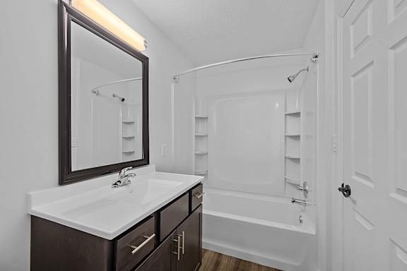 A white bathroom with a sink, mirror, and bathtub at Indian Lookout Apartments, West Carrollton, OH
