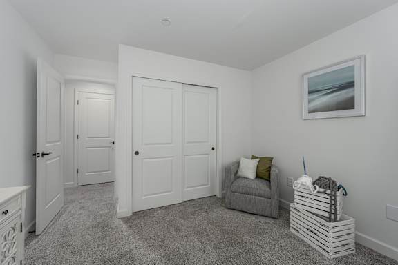A room with a grey couch, a white door, and a painting on the wall.