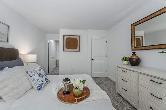 A bedroom with a bed, a tray with flowers, a mirror, and a dresser.