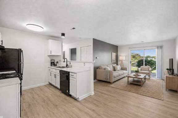 A modern kitchen with white cabinets and appliances, a dining area with a couch and chairs, and a living room with a couch and a coffee table.
