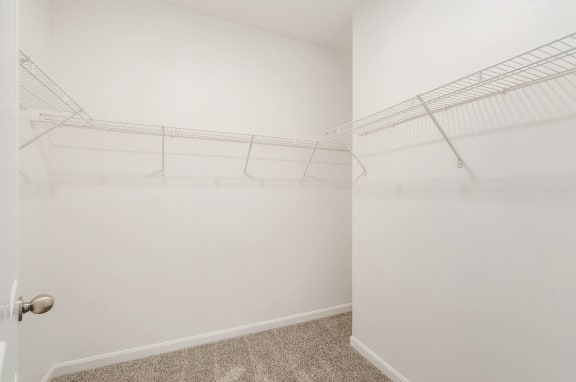 a walk in closet with white walls and shelves and a glass door