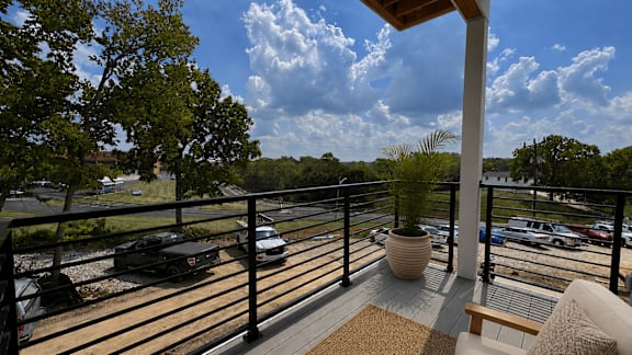 A balcony with a potted plant and a view of a parking lot.