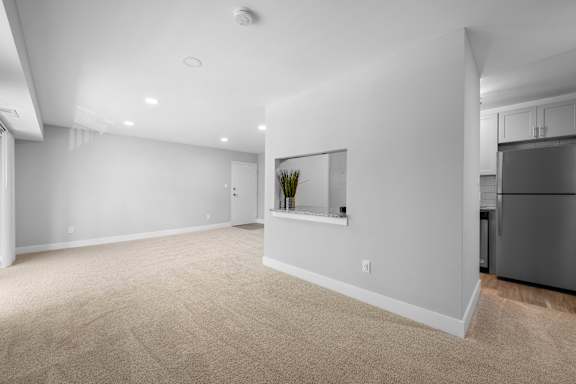 a living room with white walls and carpet and a black refrigerator at Gainsborough Court Apartments, Fairfax, Virginia