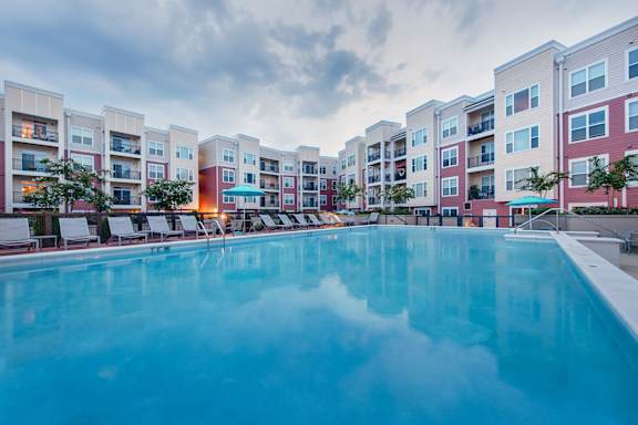 a swimming pool with lounge chairs and umbrellas in front of an apartment building