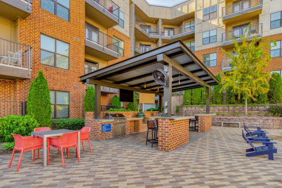 a patio with a grill and table and chairs in front of an apartment building
