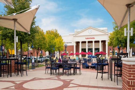 a patio with tables and umbrellas in front of a building with a clock on the