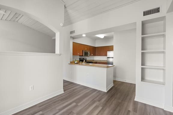 an empty living room and kitchen with white walls and wood flooring