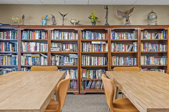A library with wooden tables and chairs in front of bookshelves.