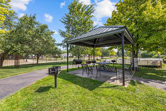 A covered picnic area with tables and chairs is surrounded by trees.