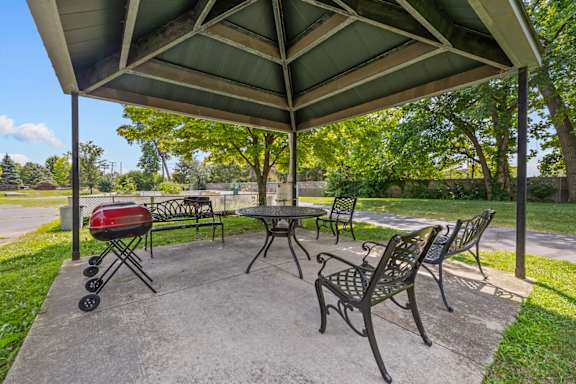A picnic area with a grill and chairs under a canopy.