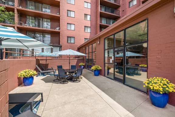 A patio with chairs and umbrellas is surrounded by a red building.