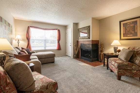 View of a living room in a one-bedroom model unit at The Lakes, showcasing furniture positioned around a fireplace.