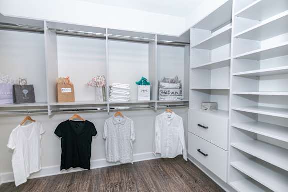 A white closet with clothes hanging and shelves.