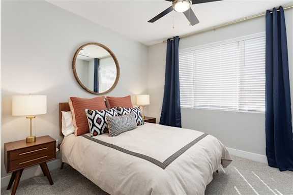 A bedroom with a bed, a mirror, and a ceiling fan.