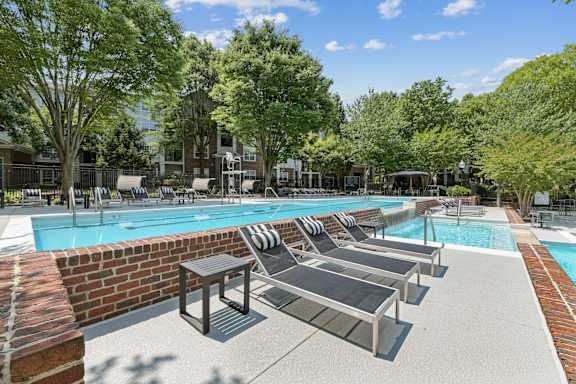 A pool surrounded by trees and chairs.