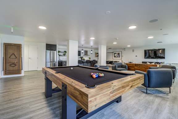A pool table is in the middle of a room with a chair and a couch.
