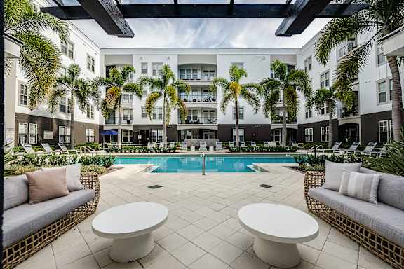 A pool surrounded by palm trees and white furniture.