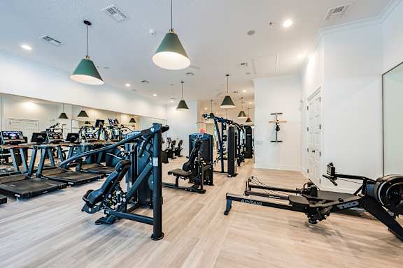 A gym with a variety of equipment including treadmills, rowing machines, and weights.