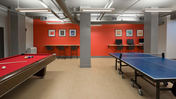 a games room with two ping pong tables and a row of tables and chairs in the