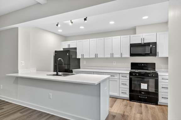 A modern kitchen with white cabinets and black appliances.