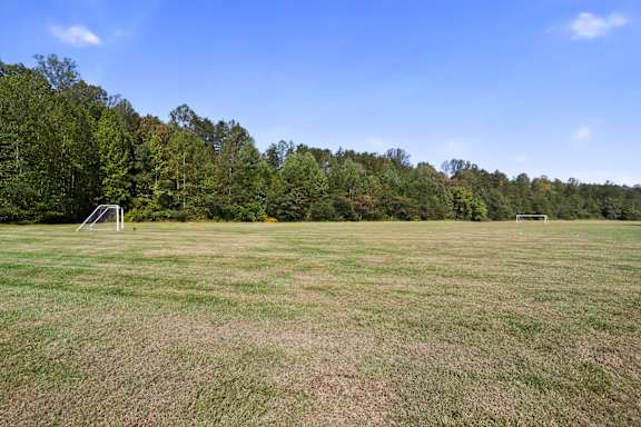 A grassy field with trees in the background and two goalposts in the middle.
