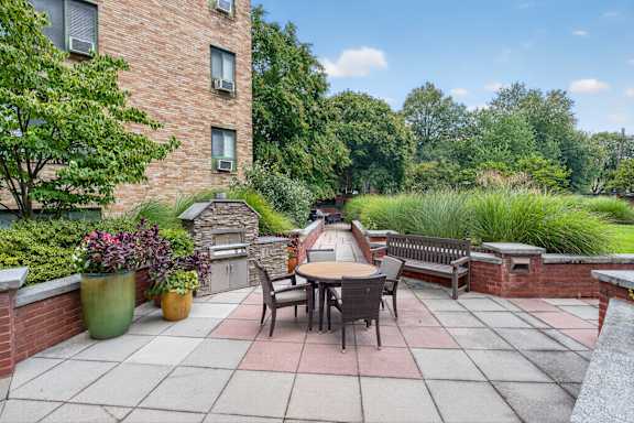 A patio with a table and chairs is surrounded by greenery.