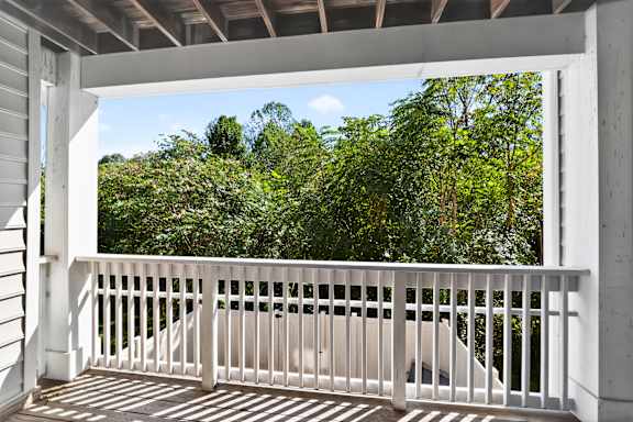 A balcony with a white railing overlooks a lush green forest.