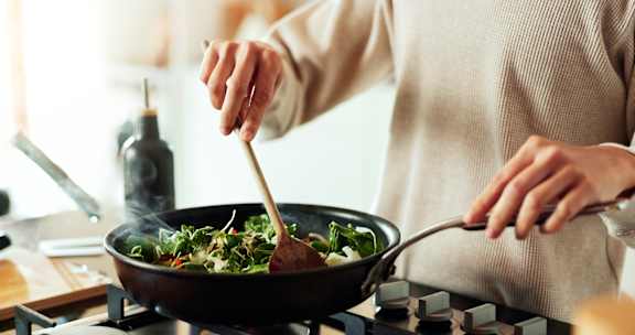 A person is cooking vegetables in a wok on a stove.