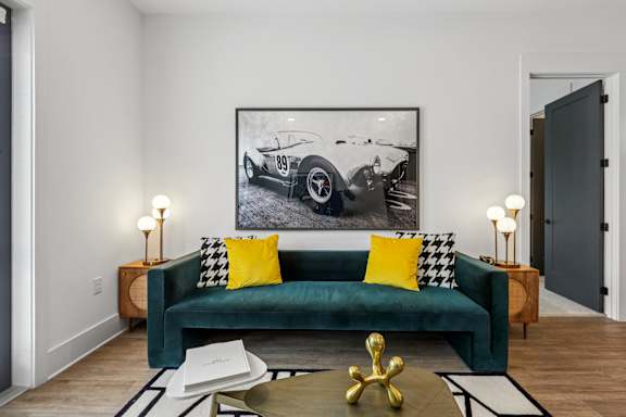 A living room with a green couch and a framed picture of a vintage car on the wall.