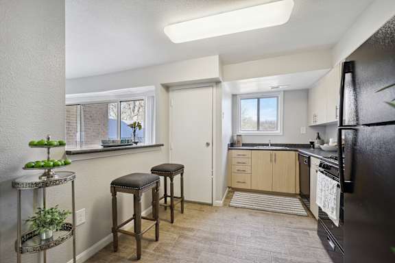 A kitchen with a black fridge, wooden bar stools, and a window with a view of trees.