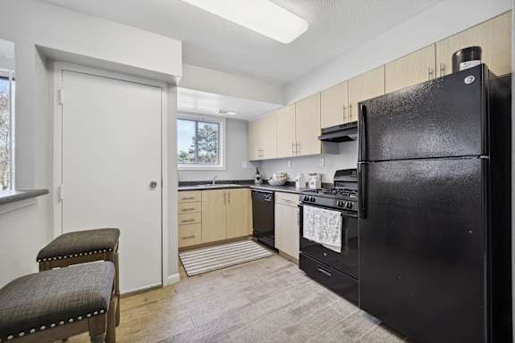 A black refrigerator is in a kitchen with wooden cabinets.