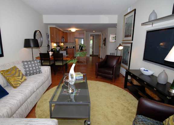 A living room with a white couch, a glass coffee table, and a television at Argent Apartments, Maryland 20910