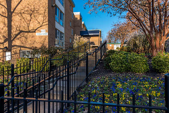 A black fence surrounds a flower bed in front of a brick building.