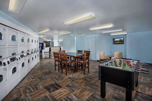 A room with a foosball table, washing machine, and dining table.