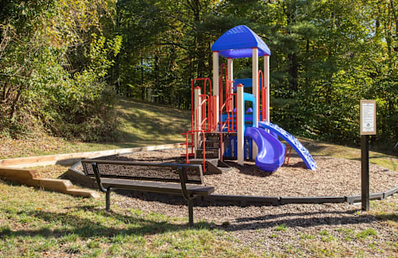 A playground with a blue slide and a wooden bench.