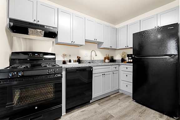A black refrigerator sits in a kitchen with white cabinets.