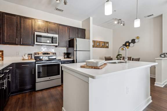 A modern kitchen with a white island and dark brown cabinets.at Century Hampton Roads, Suffolk