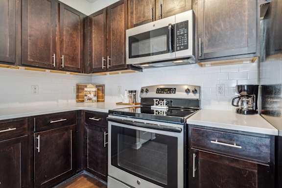 A kitchen with dark wood cabinets and a stove top oven.at Century Hampton Roads, Virginia