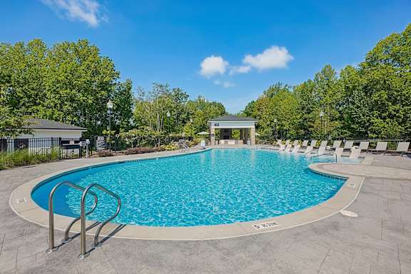 A large outdoor swimming pool surrounded by trees and a pavilion.