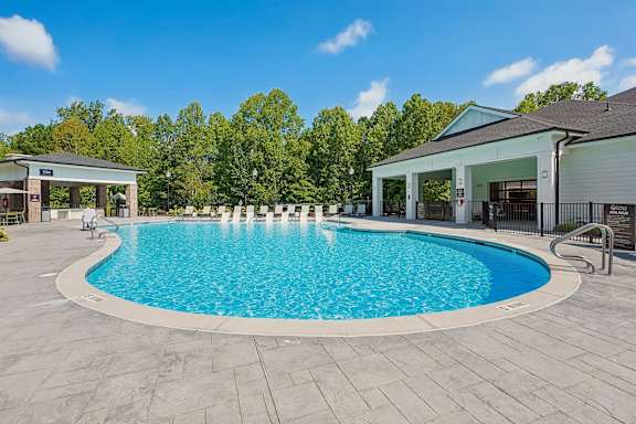 A large outdoor swimming pool surrounded by a stone patio and a covered pavilion.