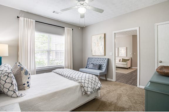 A bedroom with a bed, chair, and a ceiling fan.