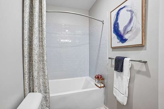A white bathroom with a blue and white painting hanging on the wall.