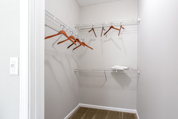 A white closet with orange hangers and a white shelf.