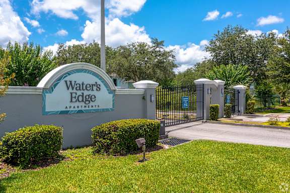 the entrance to waters edge apartments with a blue gate and green grass at Waters Edge Apartments, Lakeland, Florida