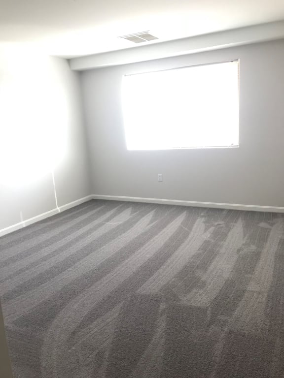 an empty room with gray carpet and a window at Carisbrooke at Manchester Apartments, Manchester, New Hampshire