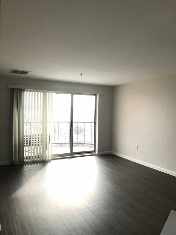 an empty living room with wood floors and sliding glass doors at Carisbrooke at Manchester Apartments, Manchester, 03102