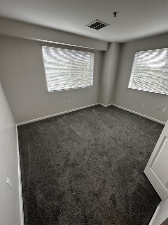 an empty room with carpet and two windows at Carisbrooke at Manchester Apartments, Manchester, NH