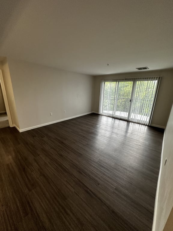 an empty living room with wood floors and a large window at Carisbrooke at Manchester Apartments, Manchester