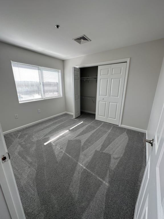 an empty bedroom with a closet and a window at Carisbrooke at Manchester Apartments, Manchester, New Hampshire