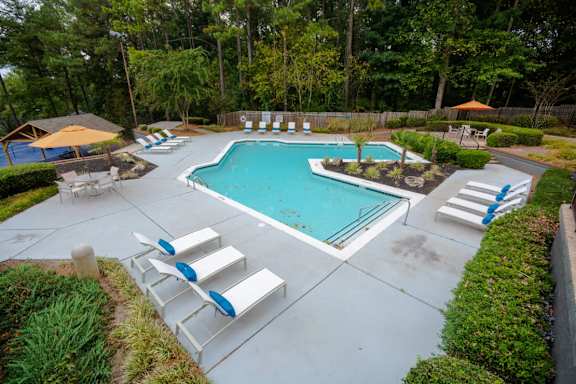 A pool surrounded by trees and a patio with chairs at The Carter 4250 Apartments, Georgia